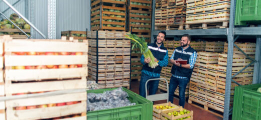 An image shows two men standing in the store, One holding some vegetables & other dairy products while they share smiles.