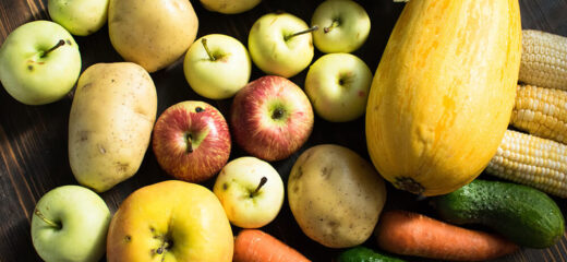 A picture of some fruits and vegetables placed on a wooden surface.