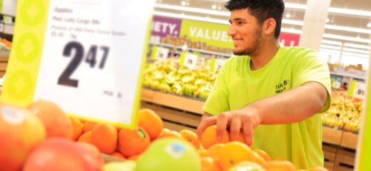 A picture of a Chalo Frescho store employee happily arranging apples in the store.