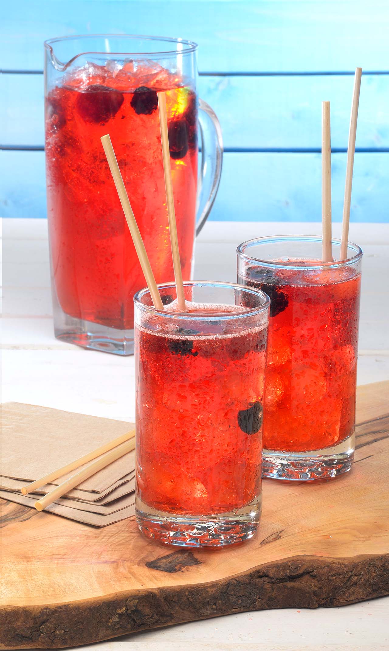 A picture of two glasses of Compliment's strawberry juice and a jug placed on a wooden tray.