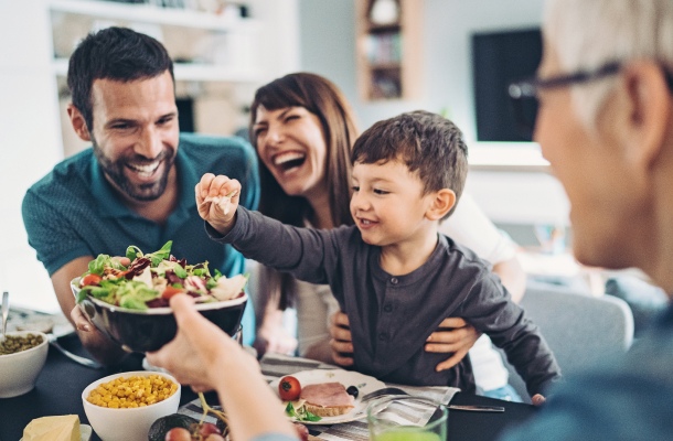 A picture of a happy family giving food to their little kid, and the kid is picking some food from the food bowl.